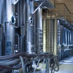 Imagem de uma instalação industrial com tanques de aço e equipamentos de processamento, ideal para indústrias de alimentos, bebidas ou produtos químicos.